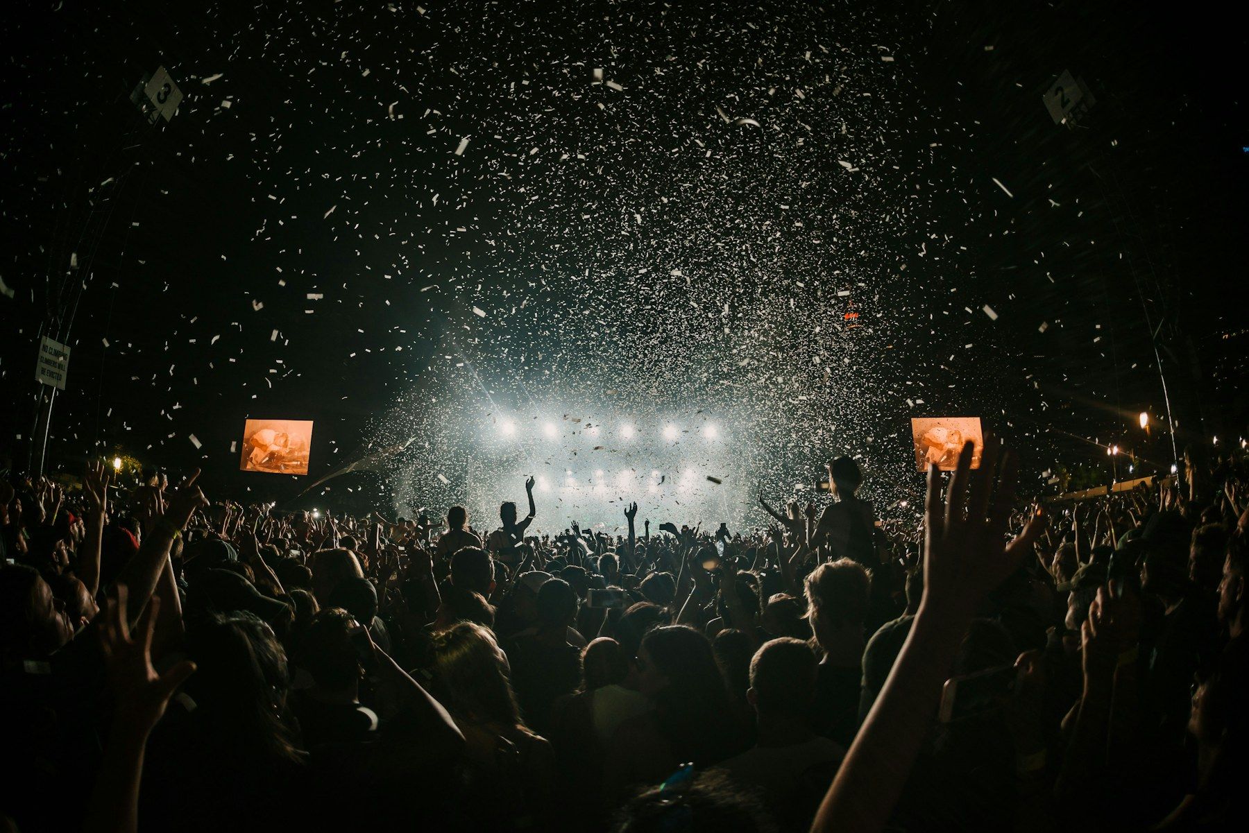 Festival crowd at night under stage lights and confetti
