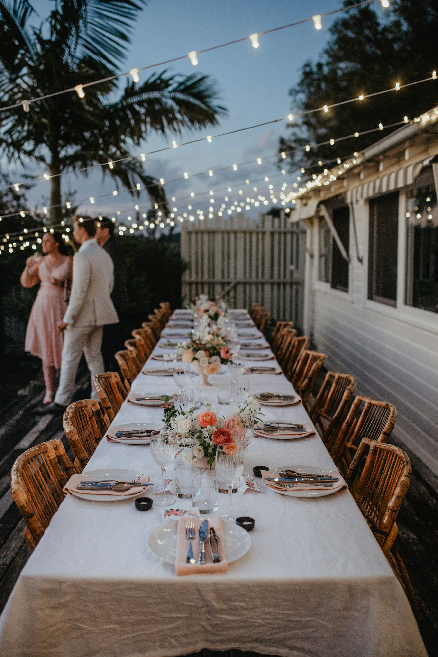 Long candlelit dinner table under string lights at dusk