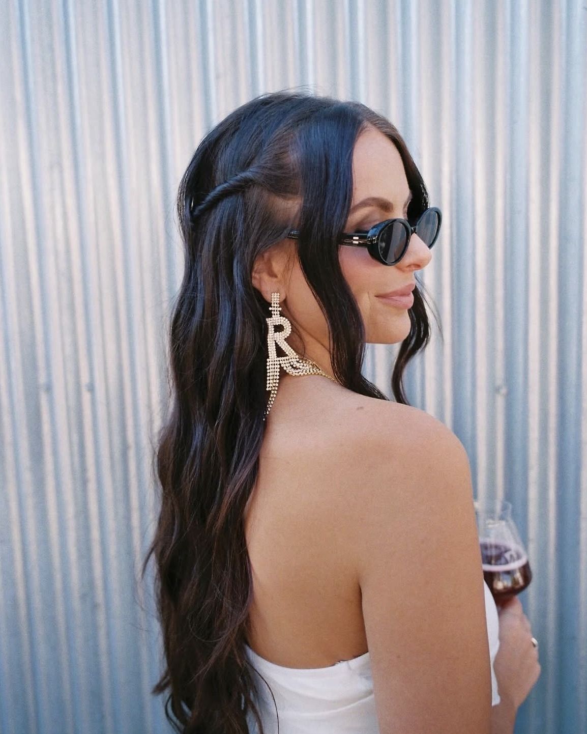 Rachel Ward in sunglasses and a white strapless top, glancing over her shoulder against a corrugated silver wall